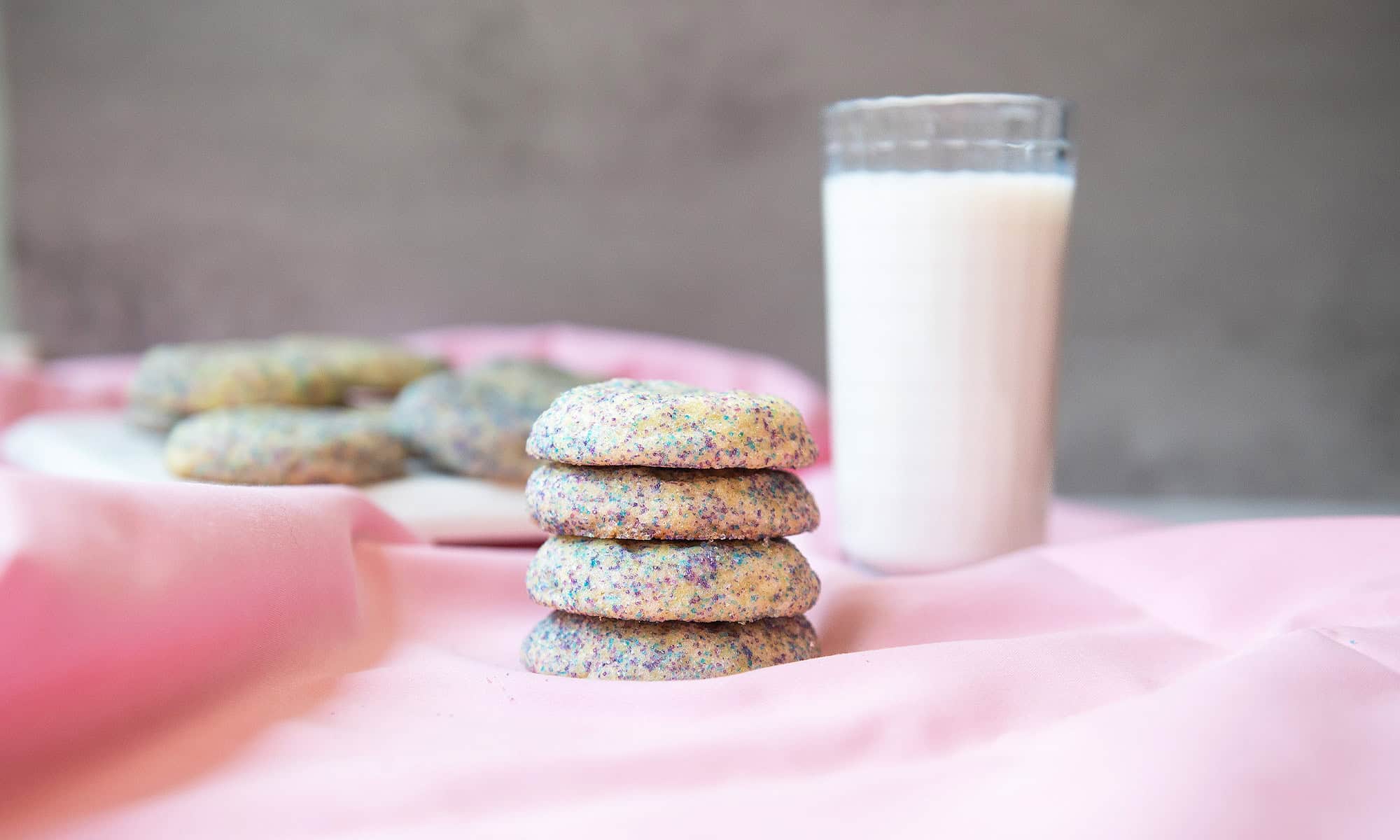 Stack of buttery soft cookies arranged on a plate against a pink background, highlighting their golden edges and tender texture.