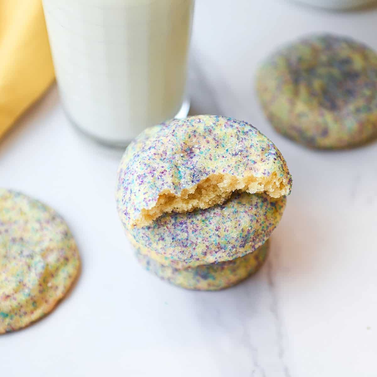 Stack of buttery soft cookies with a broken cookie on top showing the tender interior, served with a glass of milk nearby.