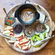 Overhead view of a caramel apple board with a mini crockpot of caramel, apple slices, and various toppings.