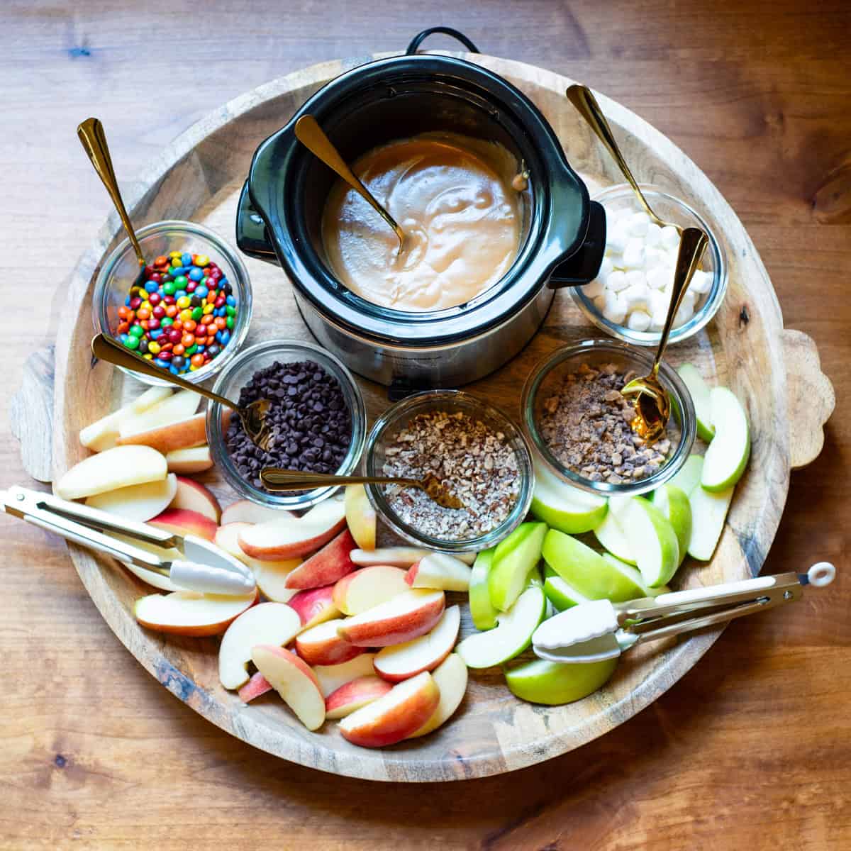 Angled view of a caramel apple dipping station with apples, caramel, and assorted toppings.