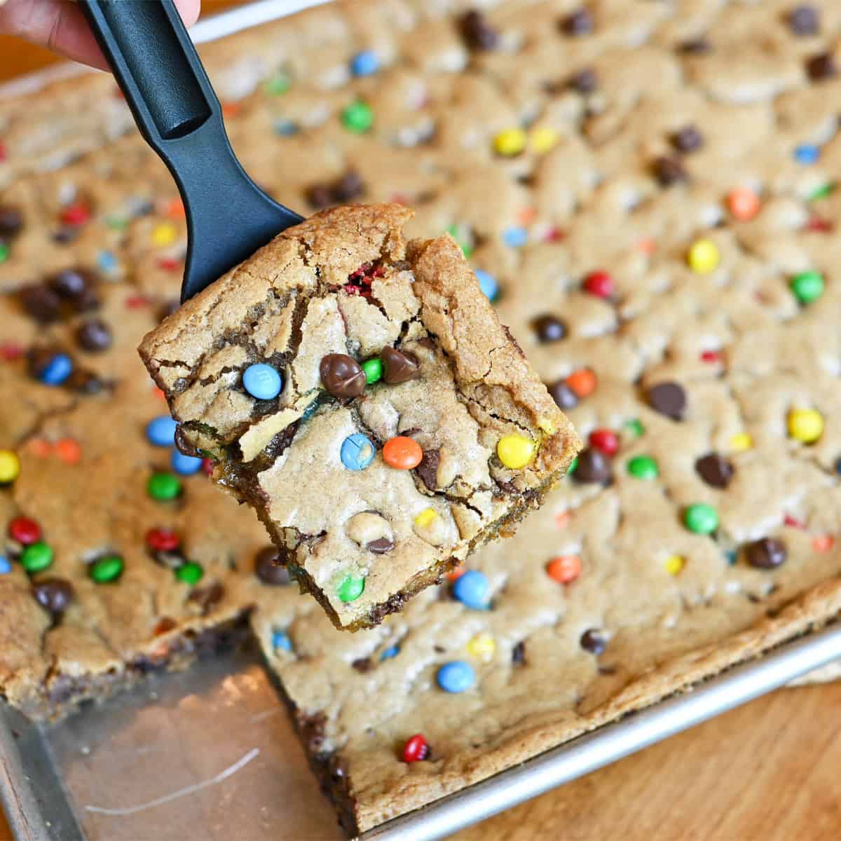 Slice of M&M cookie bar on server with full pan in background