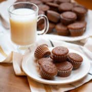 Side view of mini gingerbread muffins on a platter with a glass of milk and extra muffins on a plate