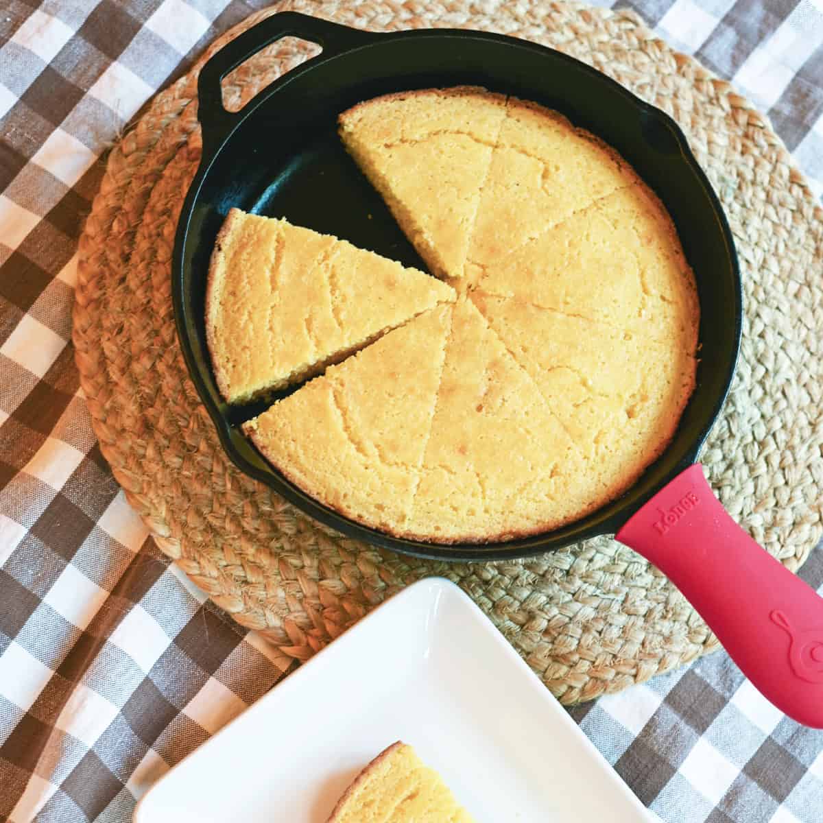 Moist skillet cornbread in a cast iron skillet with one slice cut and ready to serve