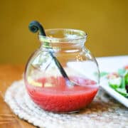 Close-up of bright red raspberry vinaigrette in a small glass jar.