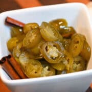 Overhead view of Cowboy Candy with cinnamon sticks in a white bowl on a wooden board
