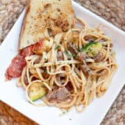 Linguini with beef and tomatoes served on a white plate, garnished with fresh herbs