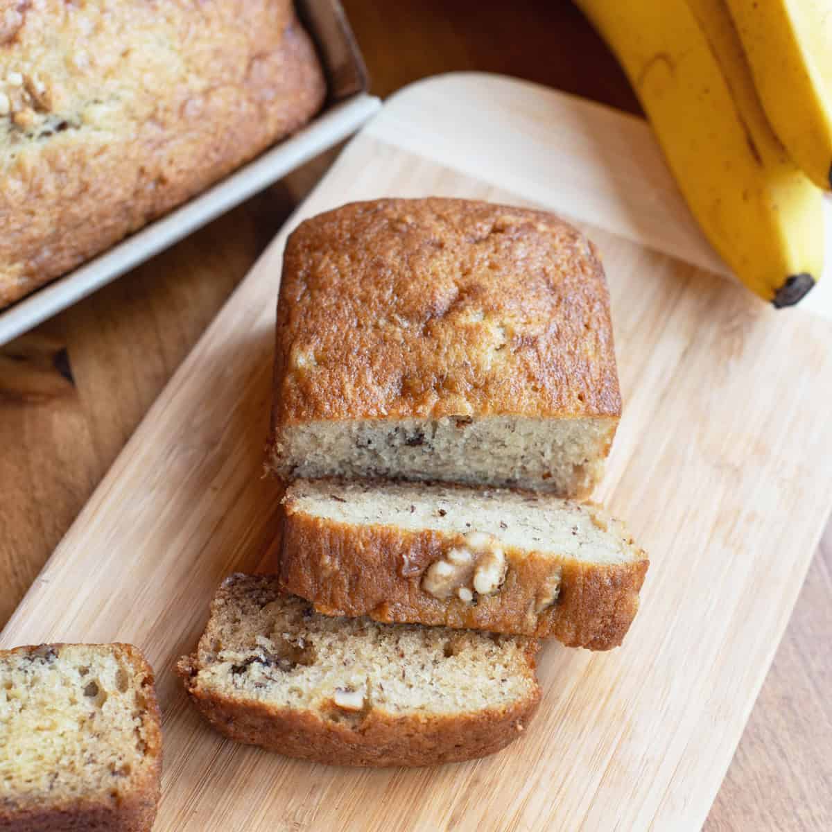 Sliced banana walnut bread on a wooden cutting board, showing a moist texture and chunks of walnuts.