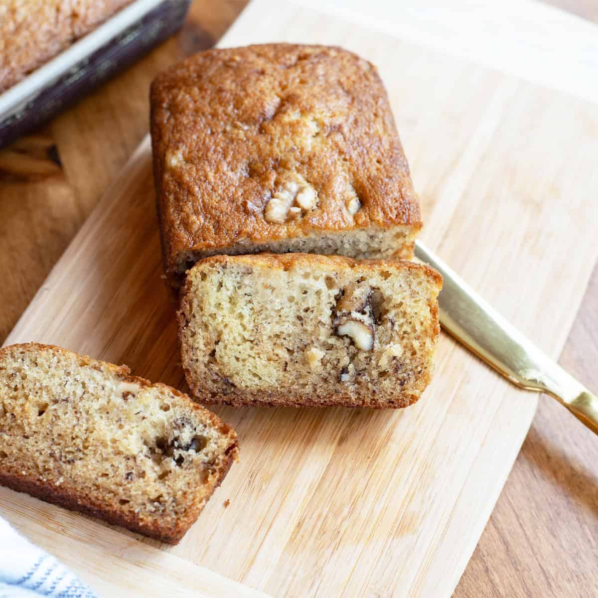 Sliced banana walnut bread on a wooden cutting board, showing a moist texture and chunks of walnuts.