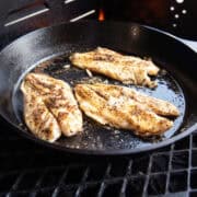 Blackened fish fillets cooked in a cast iron skillet with a dark, seasoned crust.