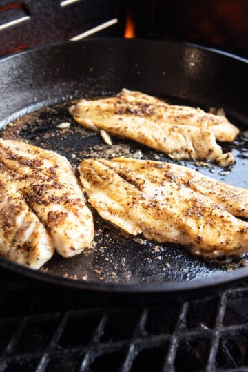 Blackened fish fillets cooked in a cast iron skillet with a dark, seasoned crust.
