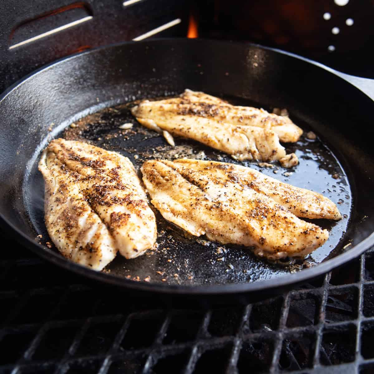 Blackened fish fillets cooked in a cast iron skillet with a dark, seasoned crust.
