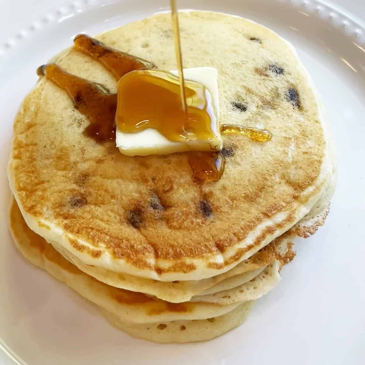Close-up of syrup pouring over butter-topped pancakes.