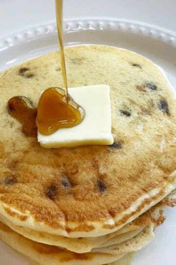 Stack of buttermilk pancakes with a pat of butter, syrup being poured over the top.