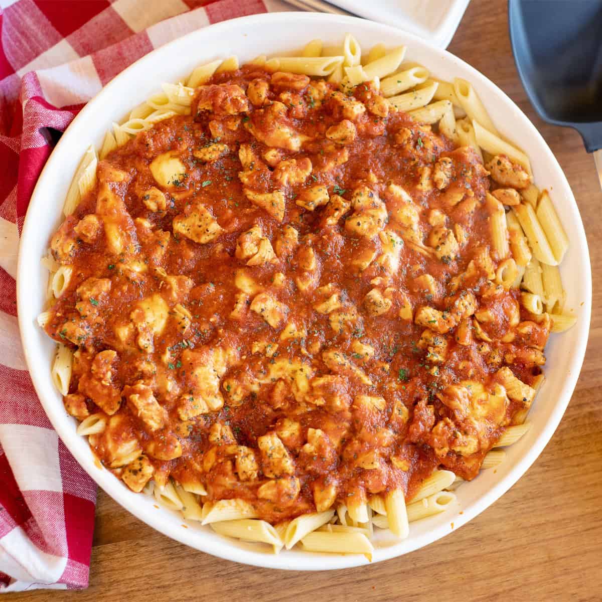 A large white bowl filled with chicken mozzarella pasta, featuring penne noodles coated in marinara sauce with melted mozzarella and pieces of chicken throughout.