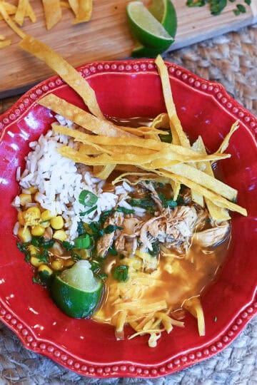 Overhead view of a soup bowl filled with flavorful soup, rice, corn, tortilla strips, shredded cheese, and a lime wedge