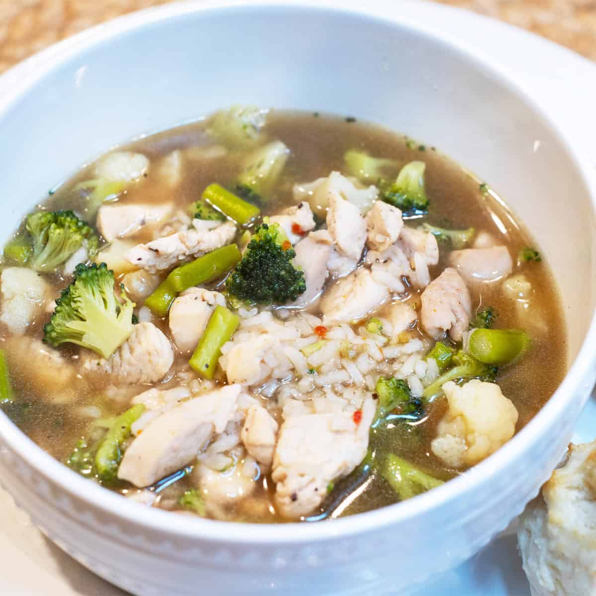 A bowl of chunky chicken soup filled with vegetables and shredded chicken, served in a white bowl on a neutral background.