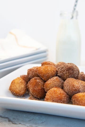 Cinnamon sugar donut holes stacked on a white plate with a glass of milk in the background