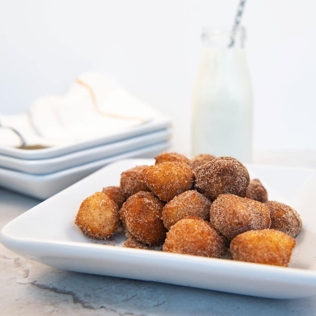 Cinnamon sugar donut holes stacked on a white plate with a glass of milk in the background