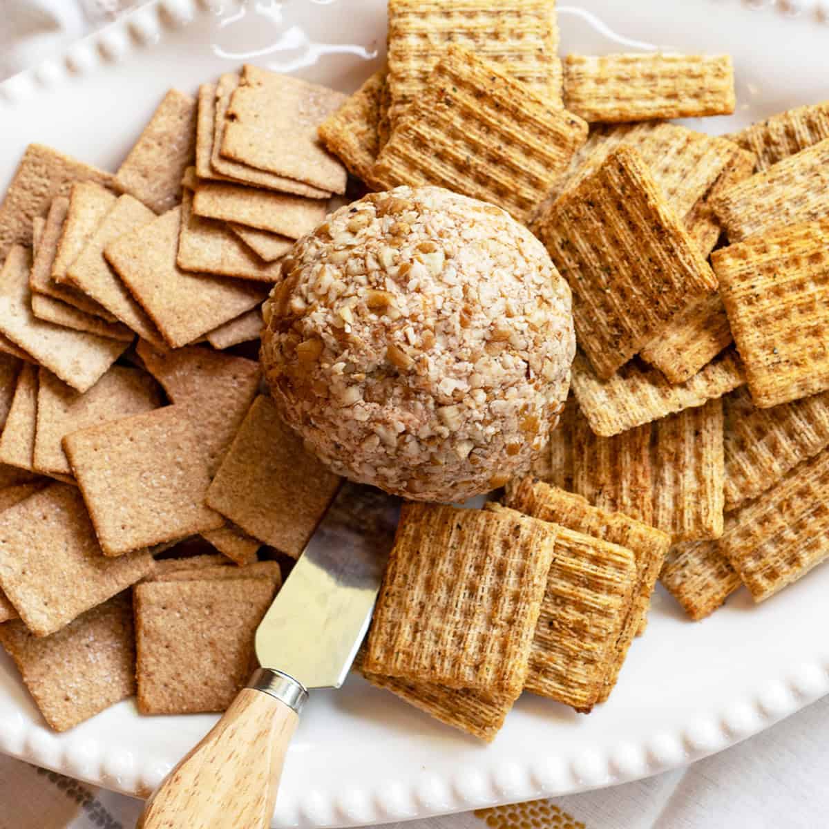 Close-up of a classic cheese ball coated in pecans surrounded by assorted crackers on a white platter.