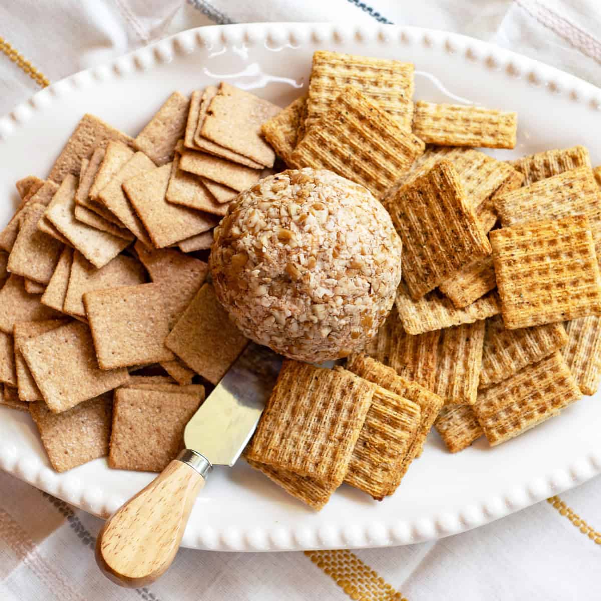 Cheese ball with assorted crackers arranged on a white serving platter.