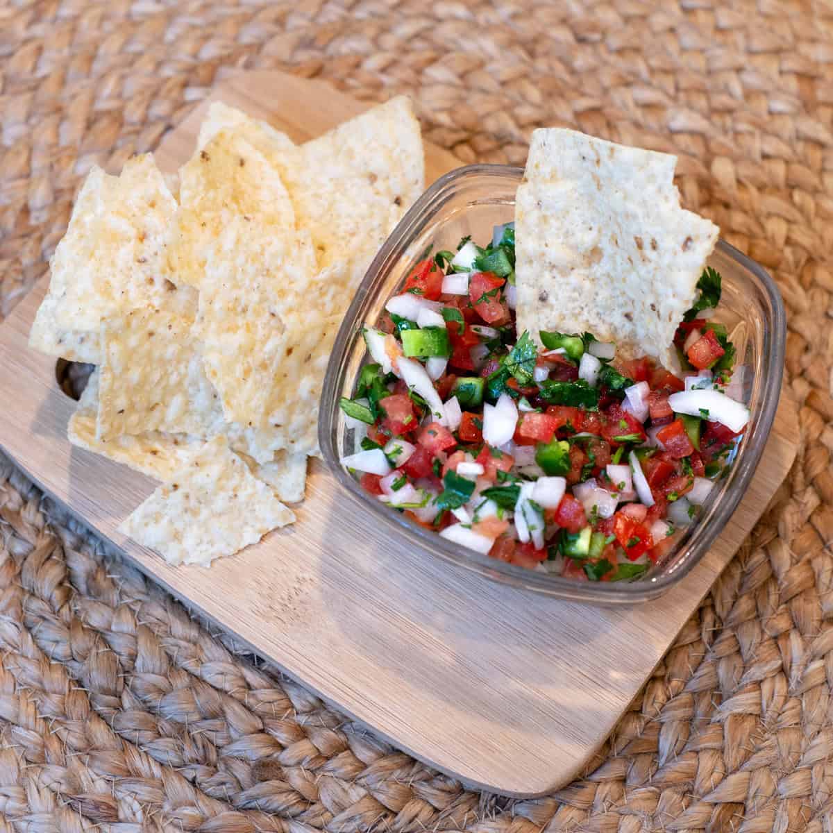 Classic pico de gallo in a small glass bowl with tortilla chips on the side.