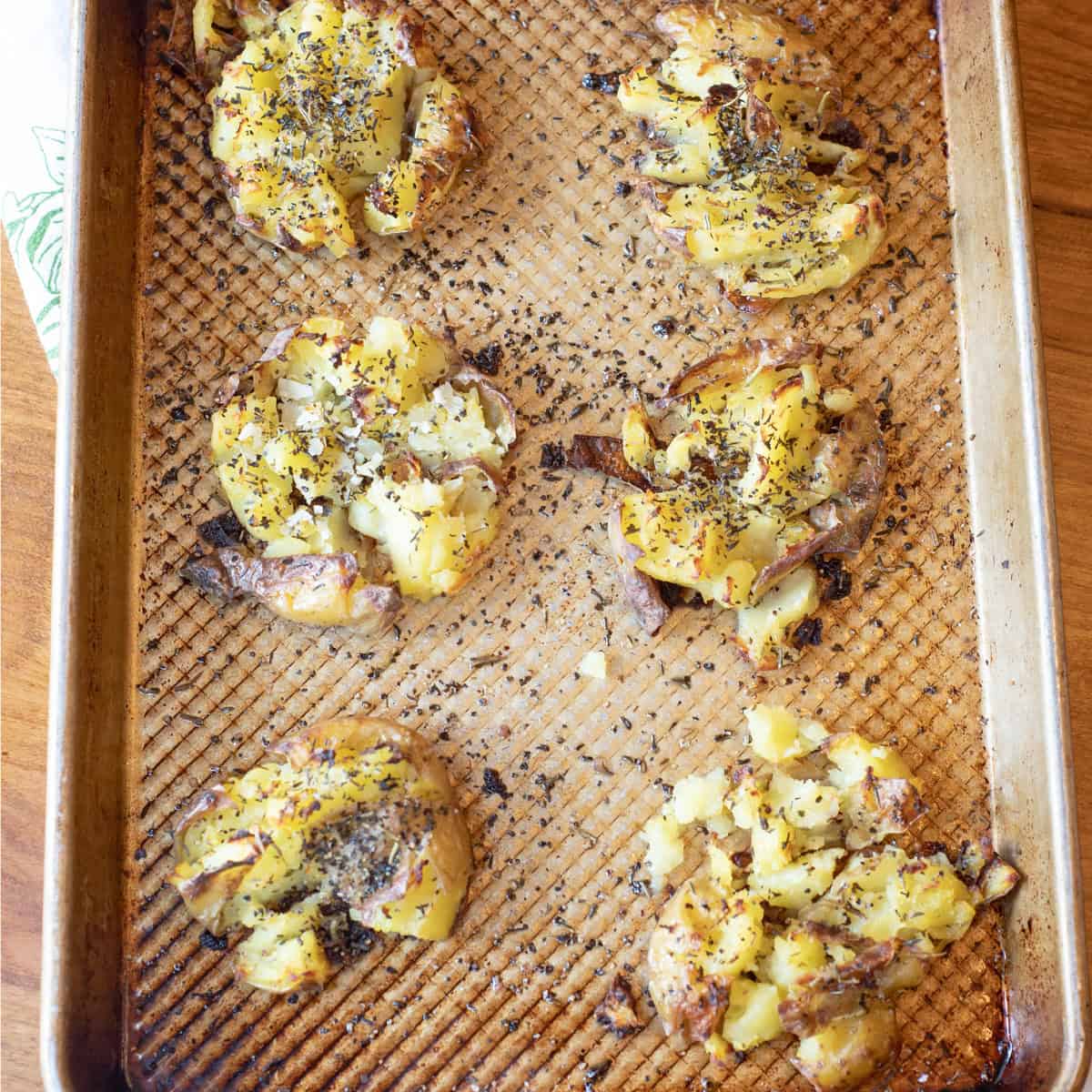 Sheet pan filled with roasted herbed smashed potatoes, garnished with fresh herbs and ready to serve.