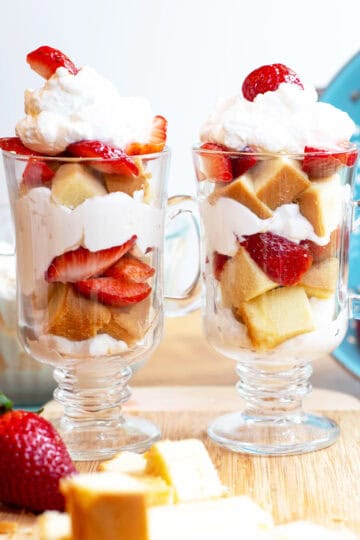 Two individual strawberry shortcake trifles in clear glasses on a serving tray, ready to enjoy.