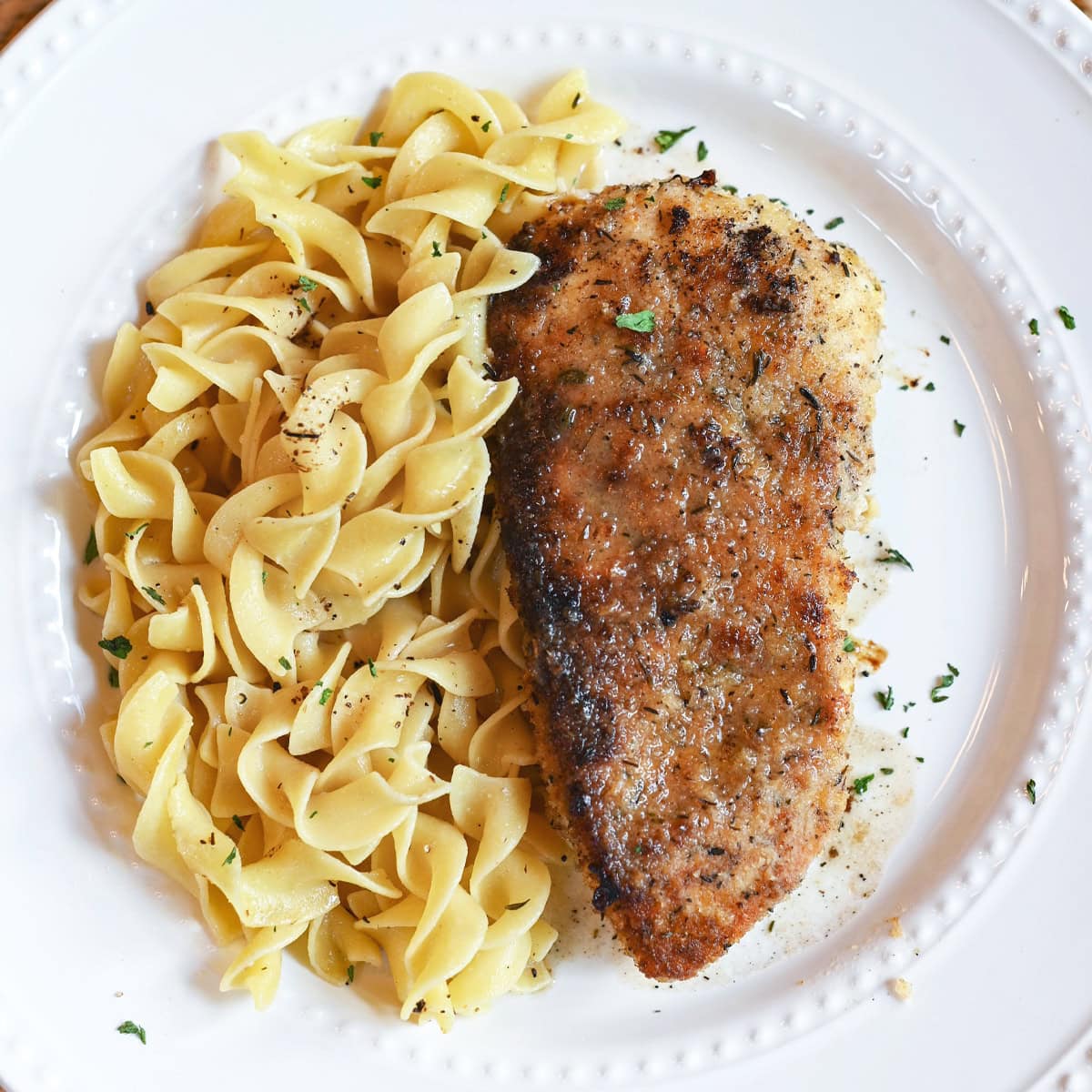 Close-up of lemon thyme chicken with golden crust and herbs, served over seasoned noodles