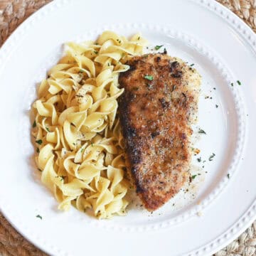 Lemon thyme chicken and egg noodles garnished with parsley on a white plate