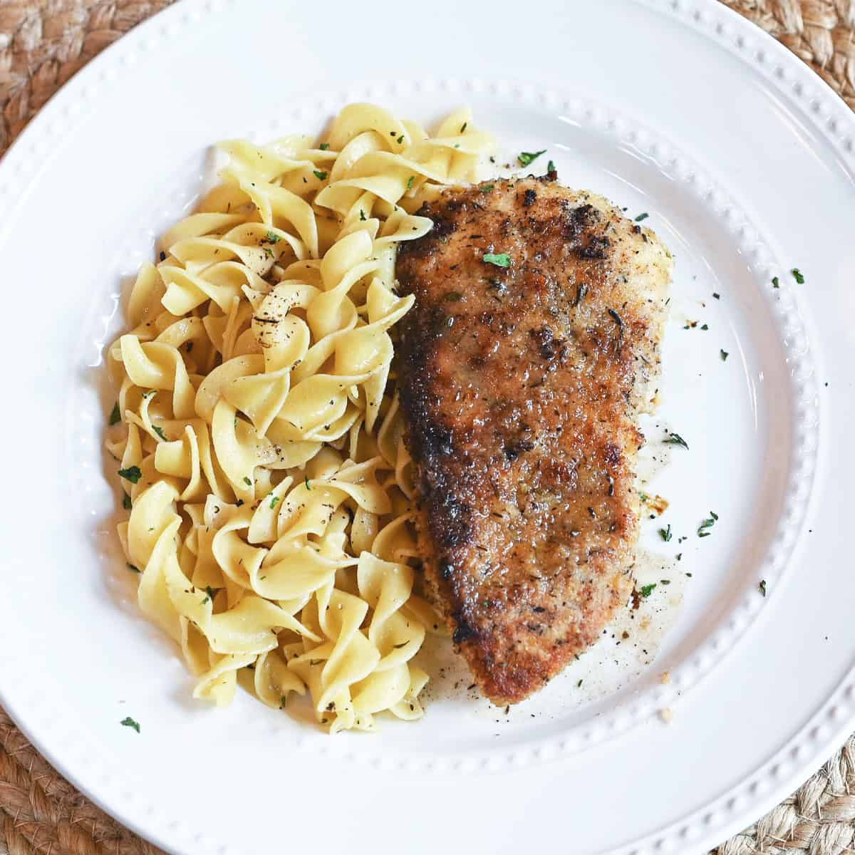 Lemon thyme chicken and egg noodles garnished with parsley on a white plate