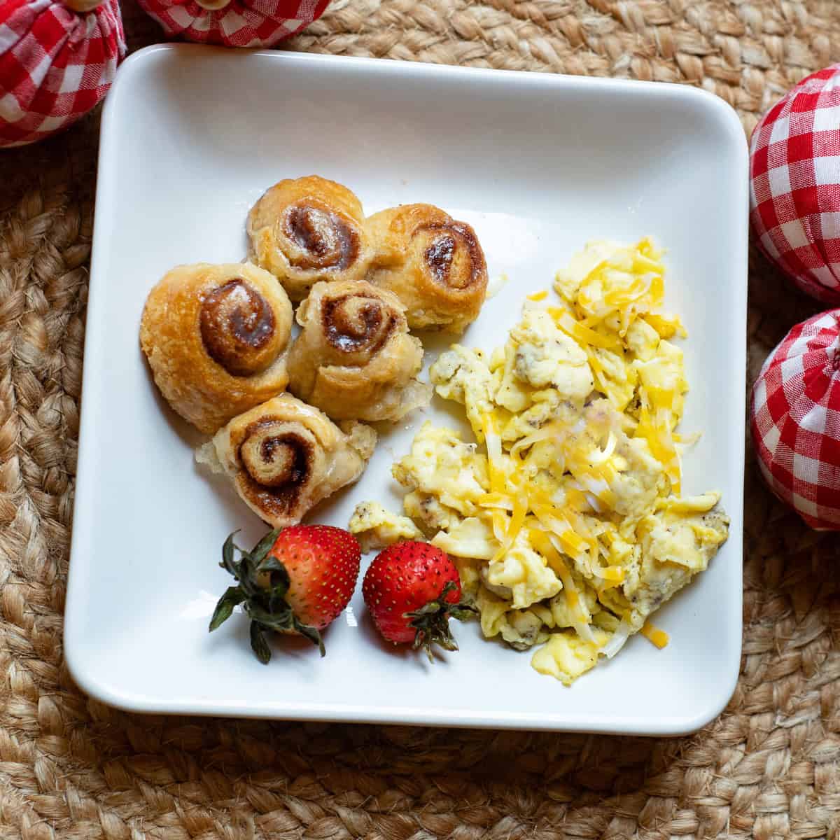 White plate with mini cinnamon rolls, scrambled eggs, and fresh strawberries.