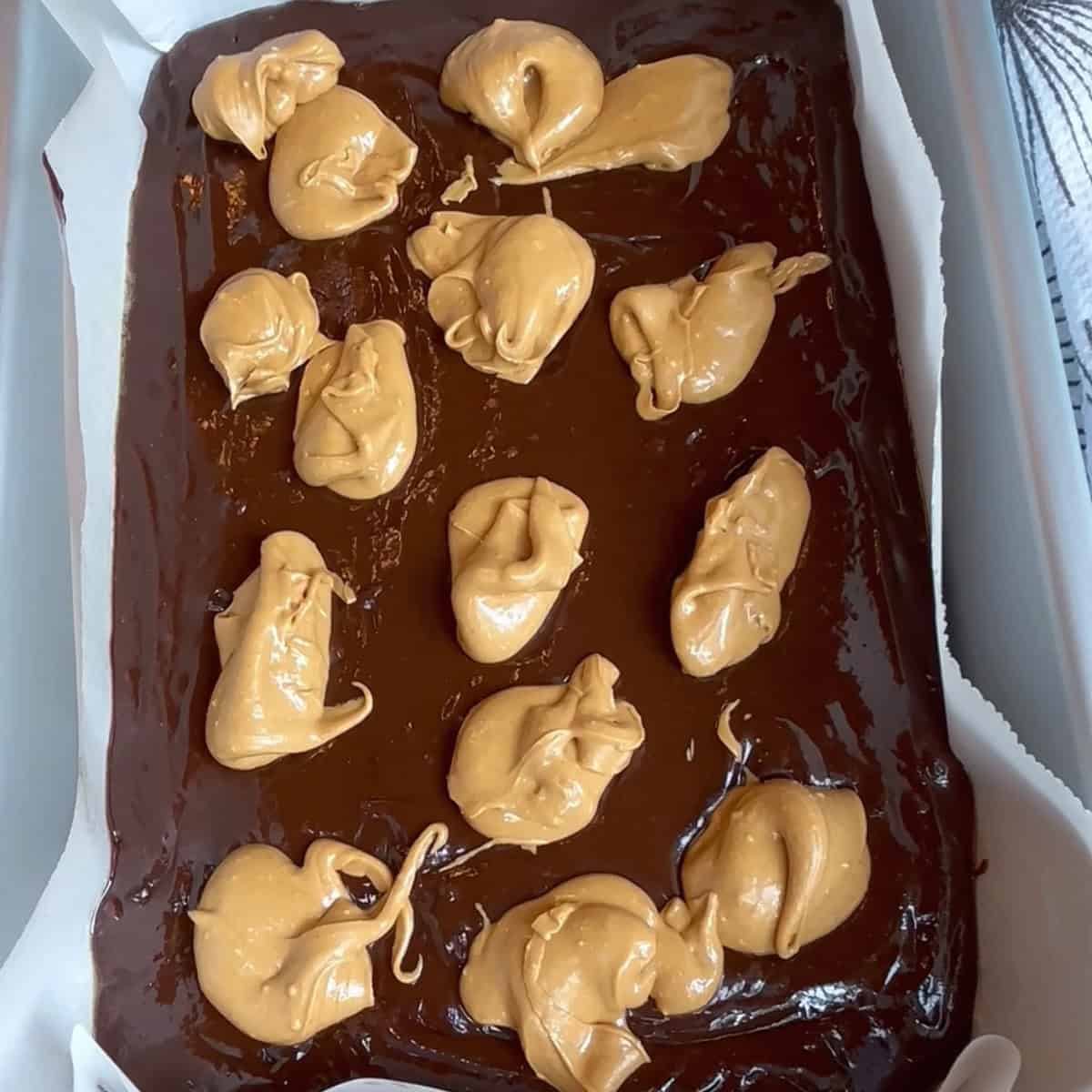 Dropping spoonfuls of peanut butter on top of brownie batter