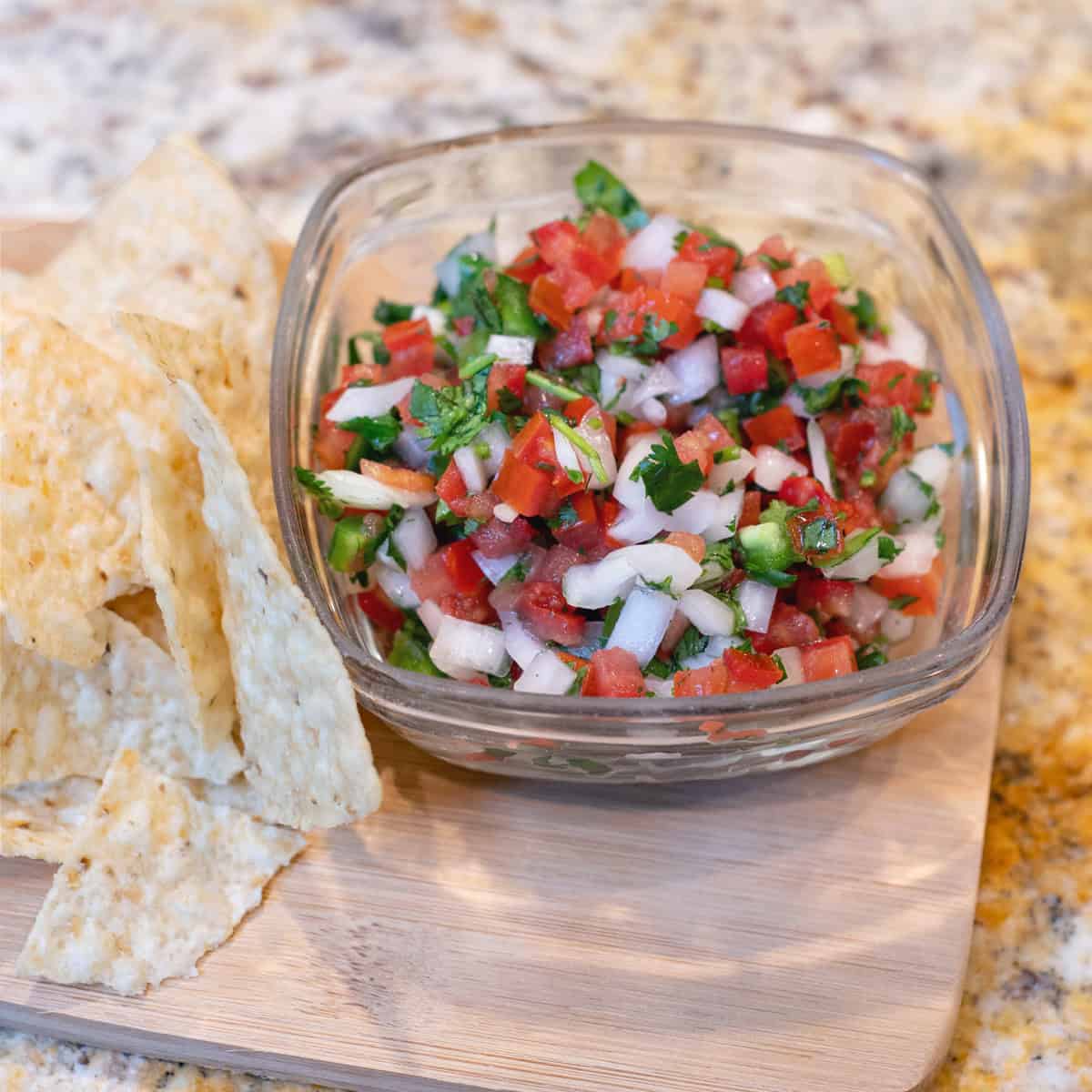 A glass bowl of pico de gallo surrounded by chips, ready to serve.