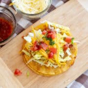 Overhead view of QuesaTacos on a wooden board topped with lettuce, cheese, and diced tomatoes.