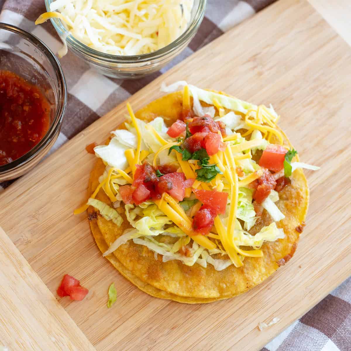 Overhead view of QuisaTacos on a wooden board topped with lettuce, cheese, and diced tomatoes.