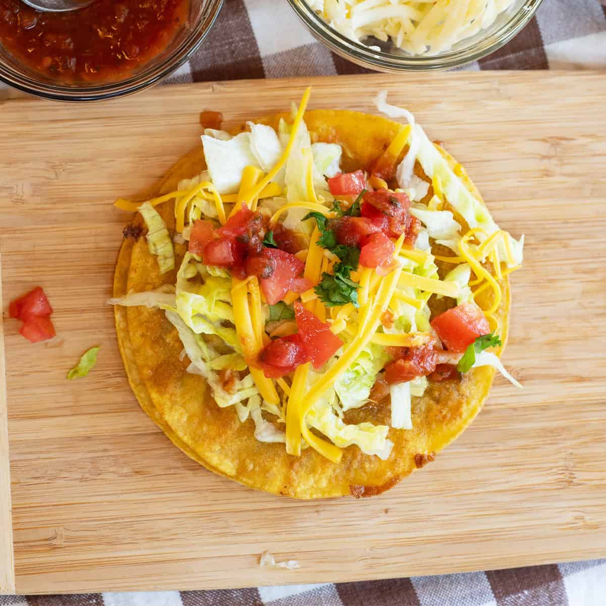 Close-up overhead shot of a QuesaTaco topped with lettuce, cheese, and tomatoes on a board.