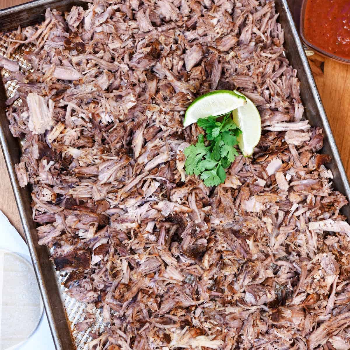 Shredded slow cooker carnitas on a pan, garnished with cilantro and lime, ready for tacos.