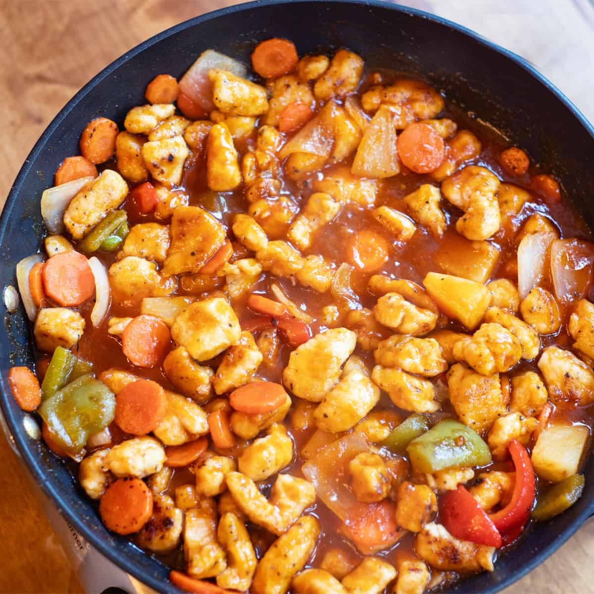 Skillet of homemade sweet and sour chicken with bell peppers and pineapple over white rice.