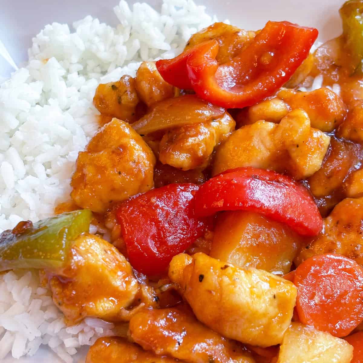 Plate of homemade sweet and sour chicken with bell peppers and pineapple over white rice.