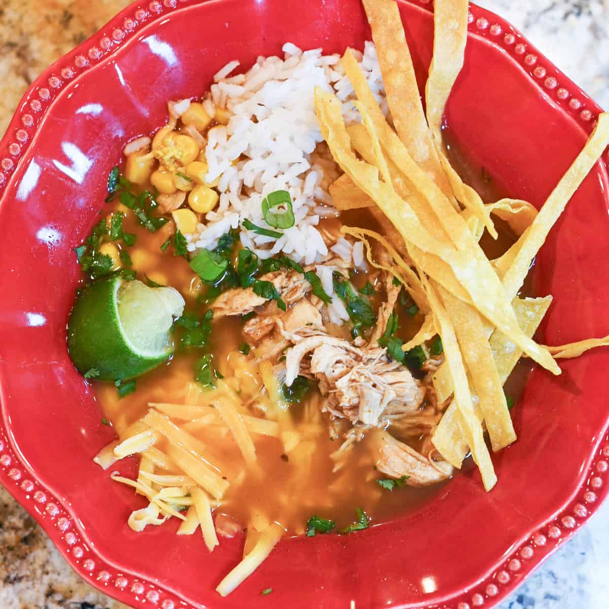 Close-up overhead view of soup bowl with visible rice, corn, melted cheese, and tortilla strips