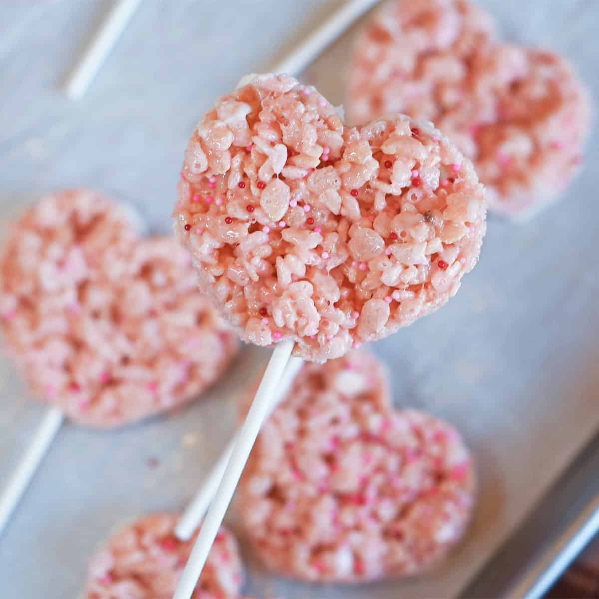 Pink Valentine Rice Krispie treat heart on a lollipop stick dipped in white chocolate