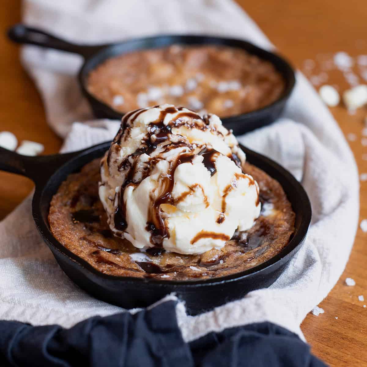 Close-up of a warm white chocolate macadamia nut skillet cookie topped with a scoop of vanilla ice cream and drizzled with caramel.