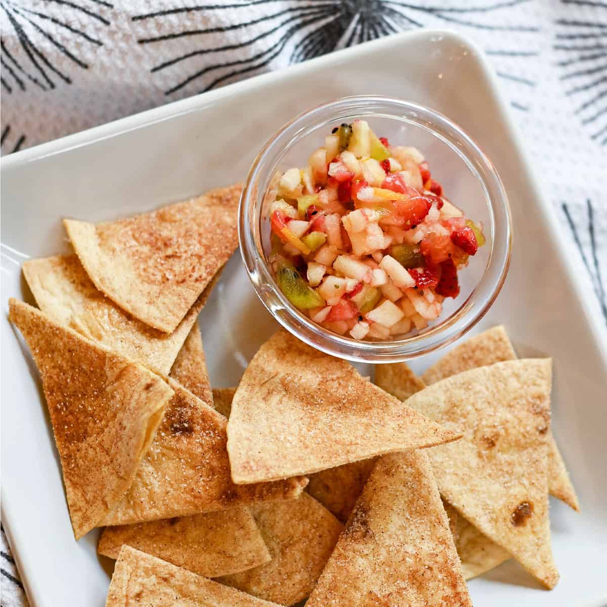 Crispy baked cinnamon chips on a white plate with a bowl of fruit salsa