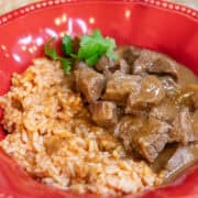Carne guisada served in a red bowl with tender beef in rich brown gravy alongside Spanish rice and warm tortillas.