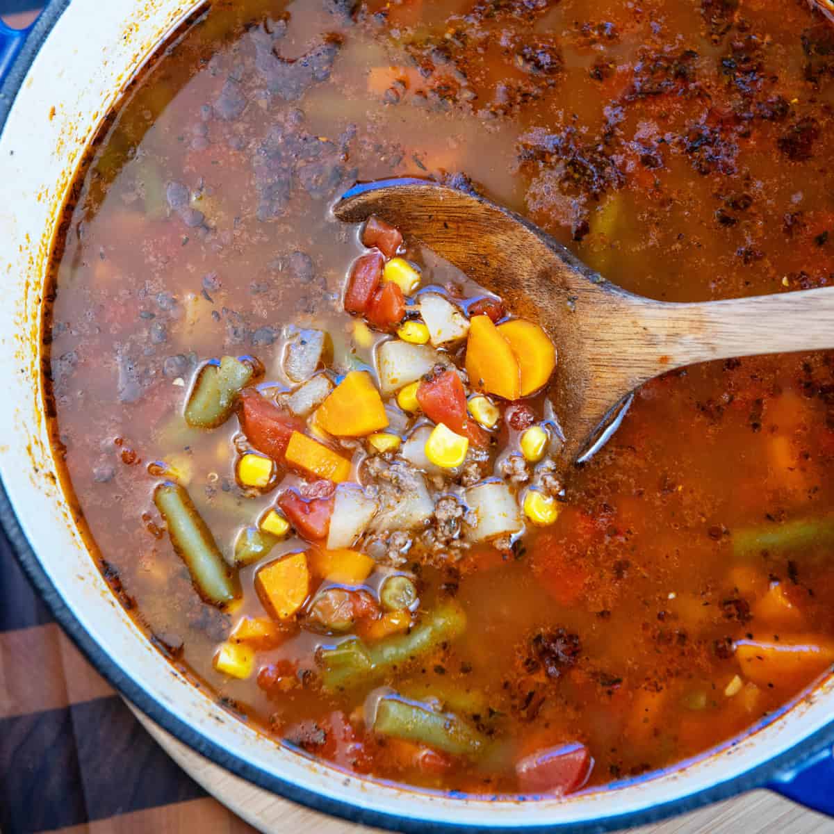 Overhead shot of a pot of beef vegetable soup with a ladle full of soup being lifted.