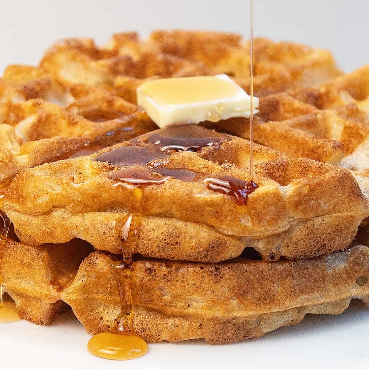 Close-up of a golden cinnamon waffle with maple syrup dripping down the edges.