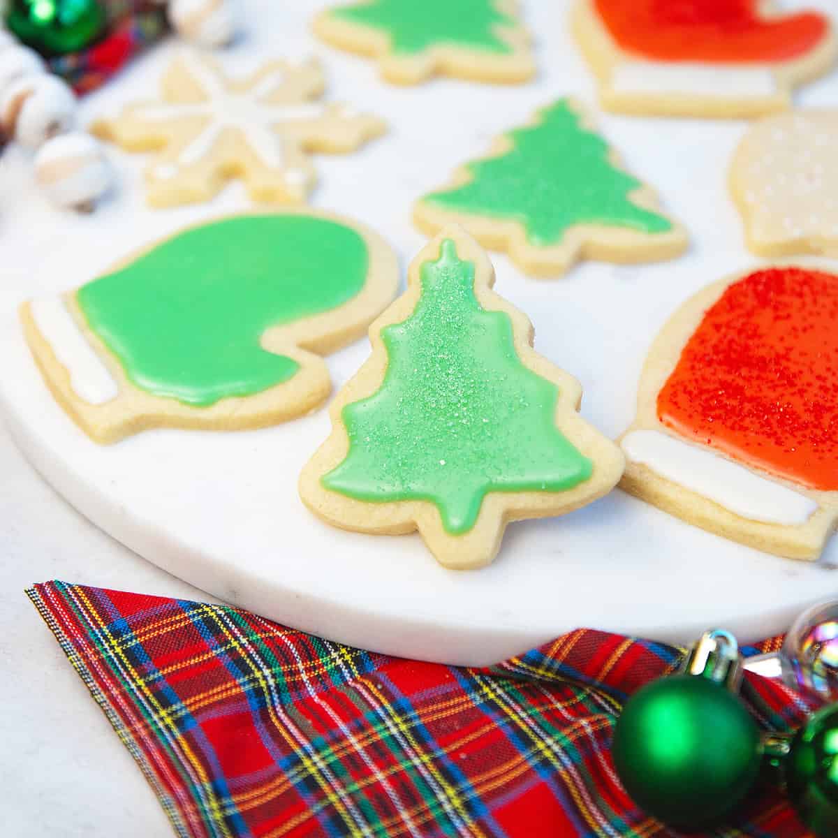 Close-up of Christmas tree sugar cookies with green icing and sprinkles on a red and green plaid background.