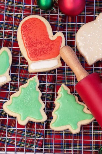 Close-up of Christmas tree sugar cookies decorated with green icing and colorful sprinkles, showing soft, buttery texture and festive detail.