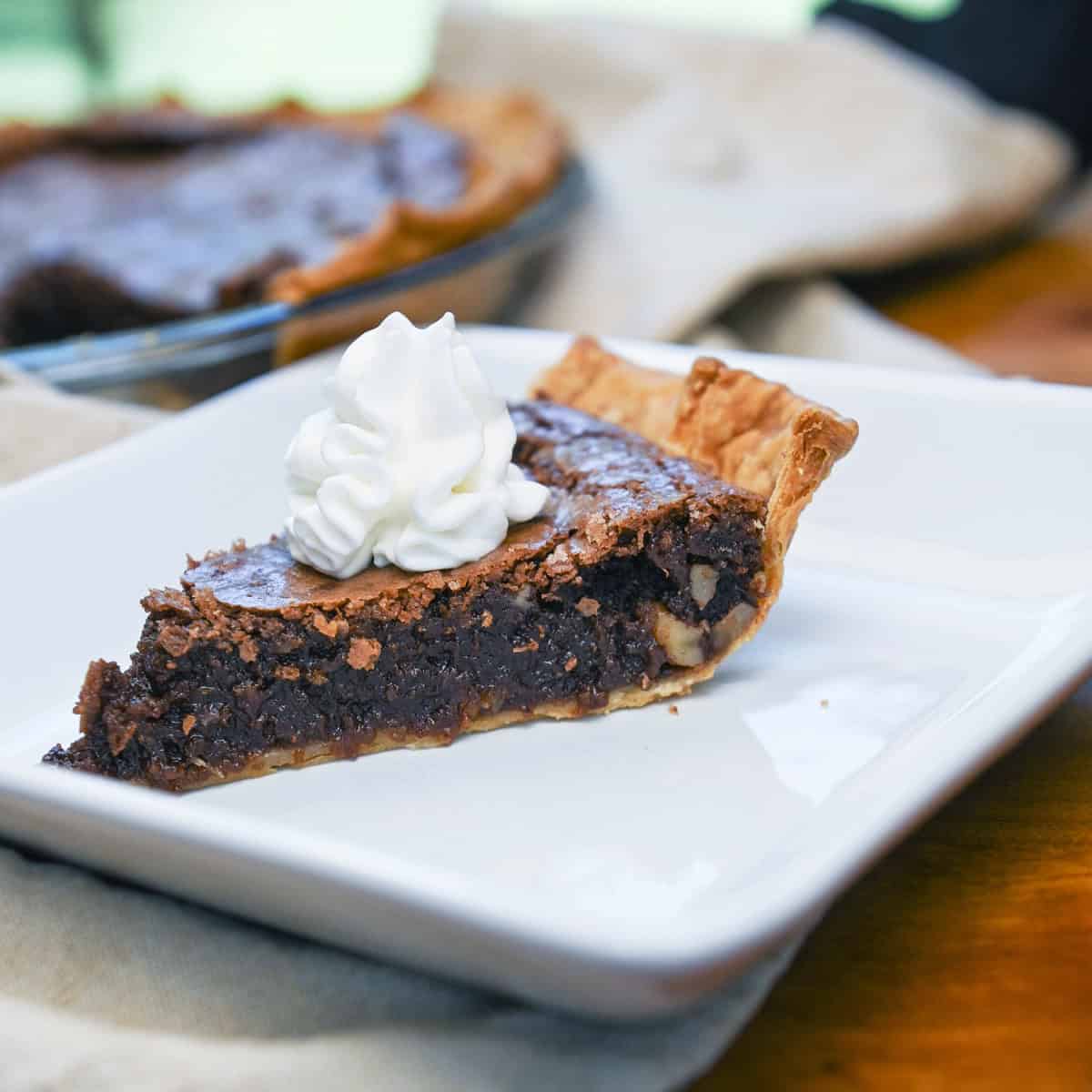 Slice of fudge pie with pecans, served on a white plate