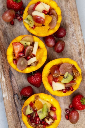 Fresh fruit salad served in hollowed orange cups on a wooden tray